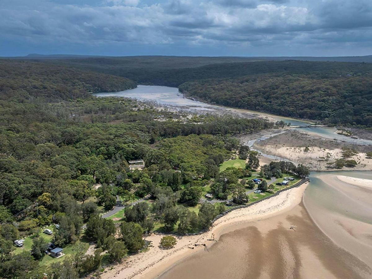 An aerial view of Bonnie Vale campground surrounded by bush and next to Hacking river and beach in