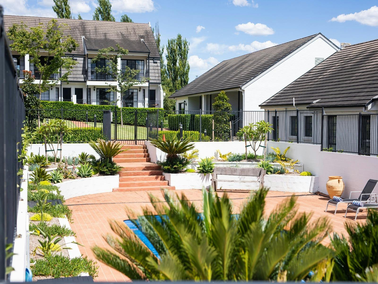 A scenic view of a backyard showcasing a pool and a house, along with accommodation rooms nearby.