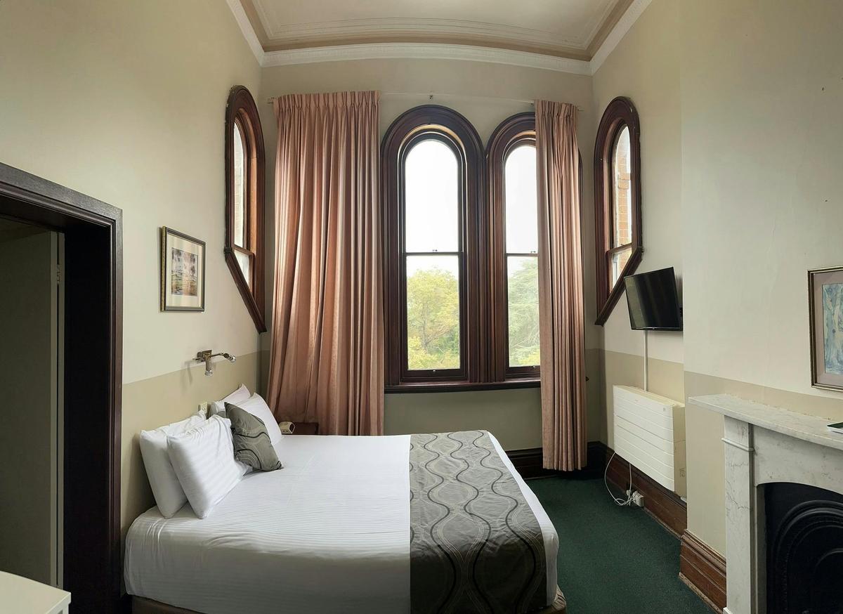 A mid shot of a king bed and a window letting light into the room