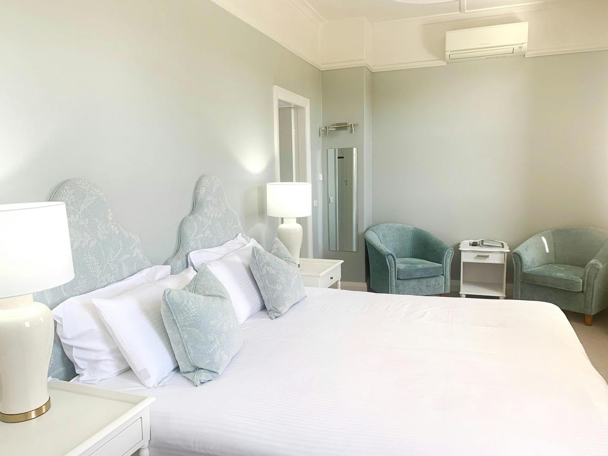 A white king bed takes up the frame, with green chairs in the background