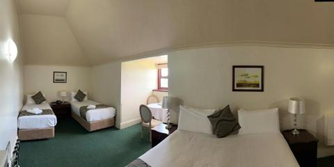 A wide shot of a large room, with two singles and a king bed. There is a table and chairs.