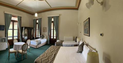 A wide shot showing a king bed and two singles, along with a table and chairs.