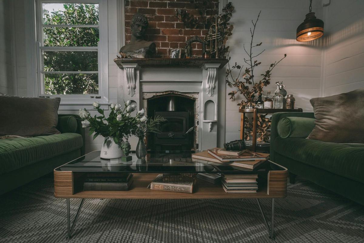 Cosy lounge room with fire place, green velvet sofas and lots of  interesting books
