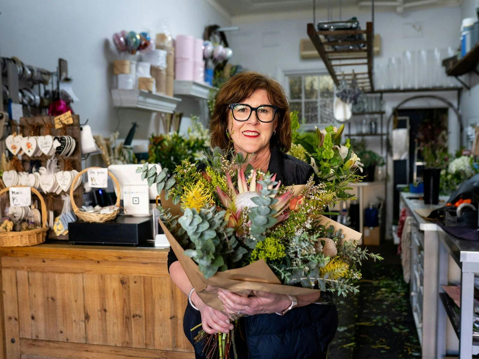 a shop owner holding a floral arrangement she has crafted
