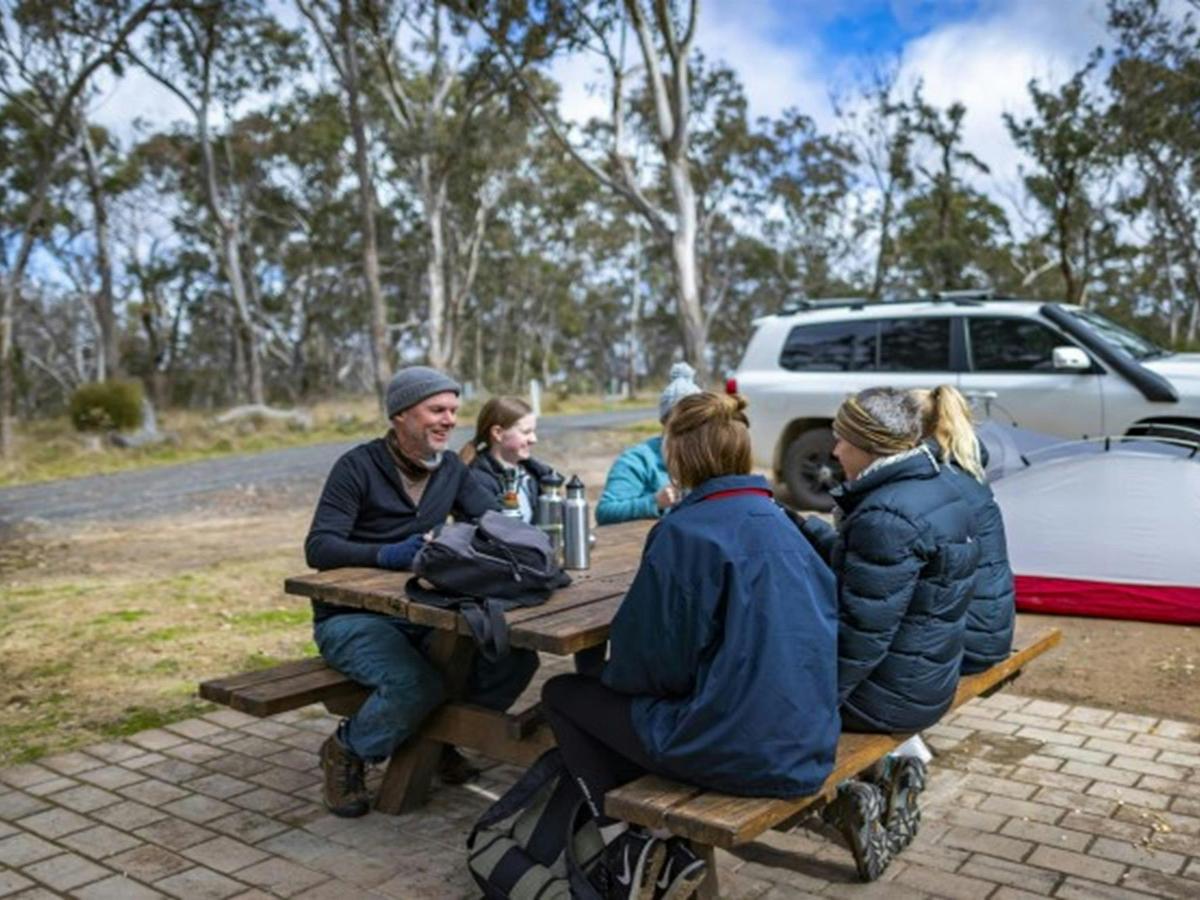 A group of friends sitting at a picnic table with their tent in the background at Dangars Gorge
