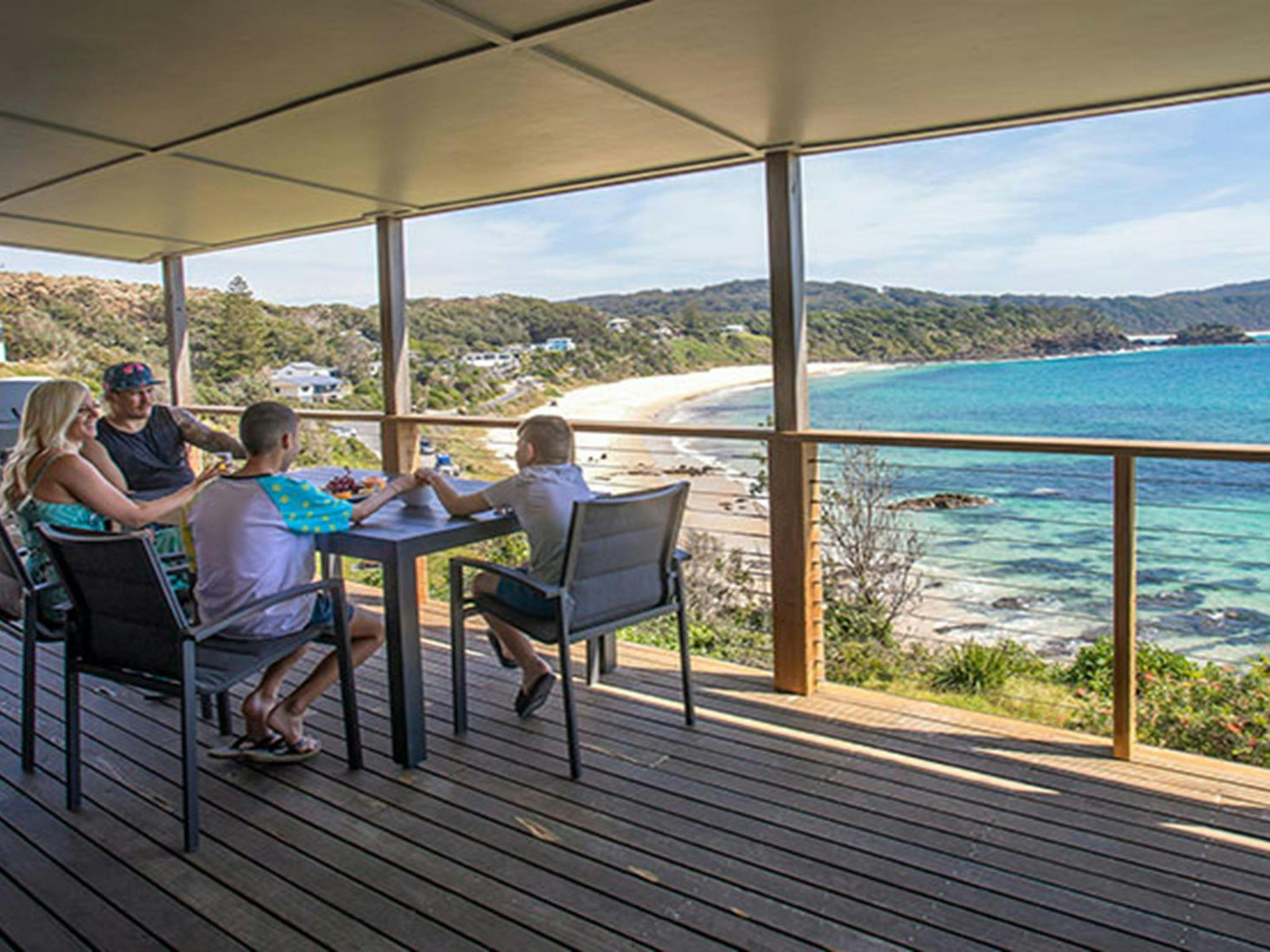 A family on the deck of Davies Cottage with Boat Beach and Sugarloaf Bay in the background. Photo: