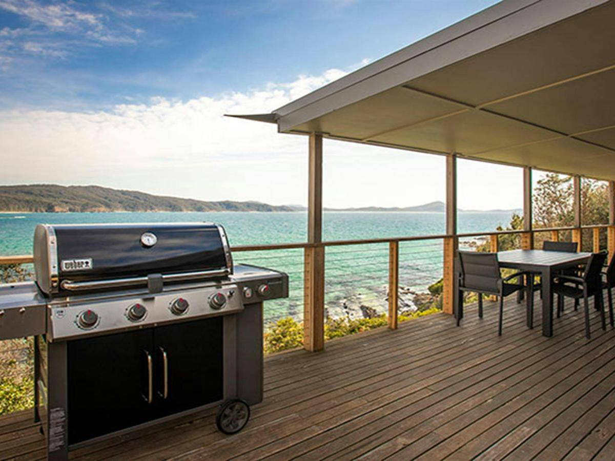 A gas barbecue and outdoor seating on the deck of Davies Cottage, with Sugarloaf Bay in the