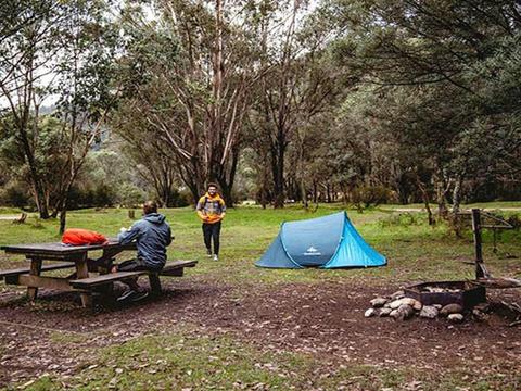 A man sits at a picnic table next to a tent at Geehi Flats campground, Kosciuszko National Park.