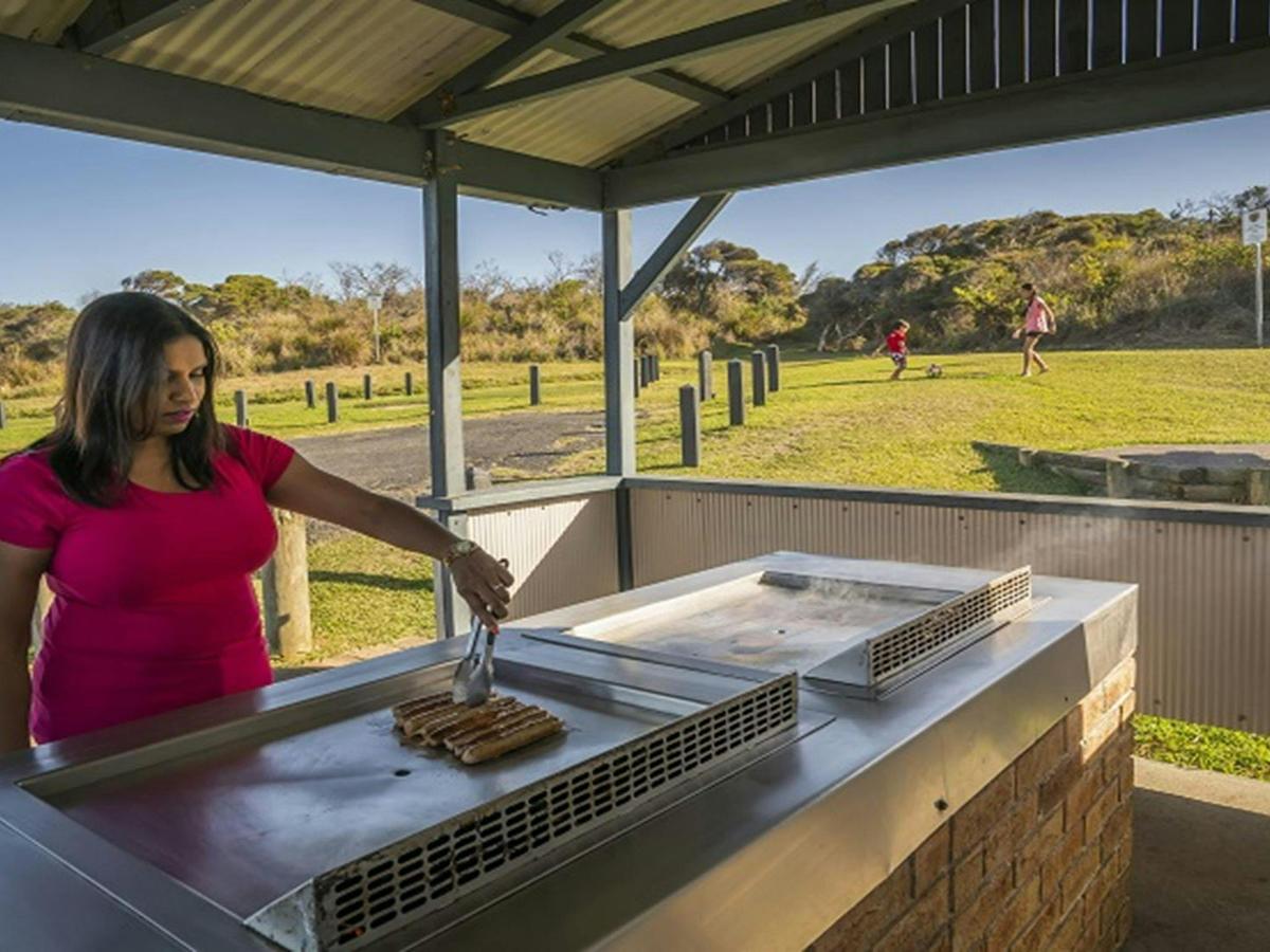 An adult cooking lunch on the barbecue and children playing soccer nearby, Frazer campground,