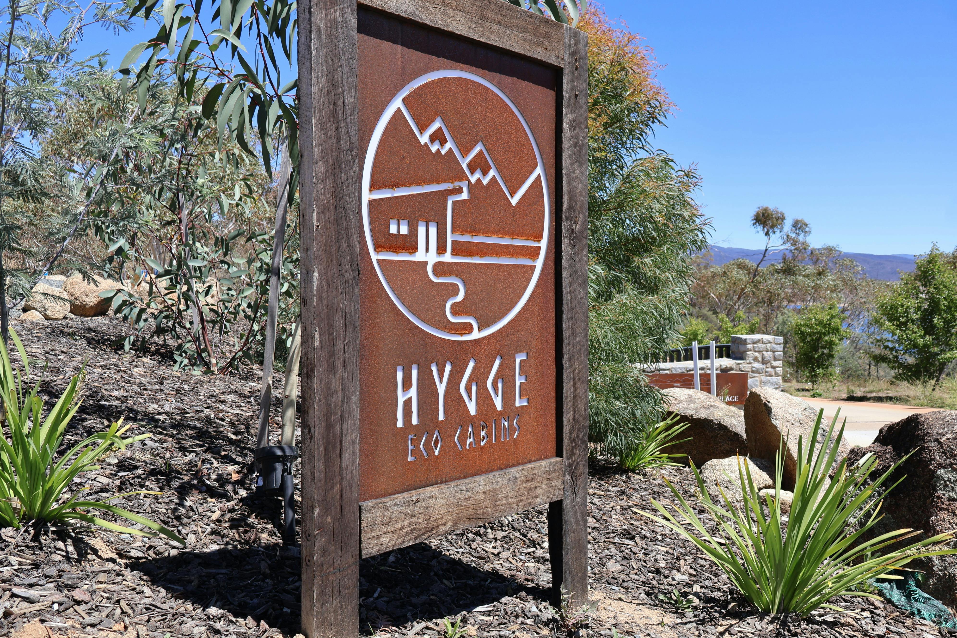 A sign with the word Hygge appears in the foreground, behind it there is Australian bush scenery.