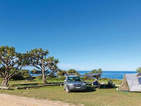 A tent pitched next to a car with the beach in the background at Red Cliff campground in Yuraygir