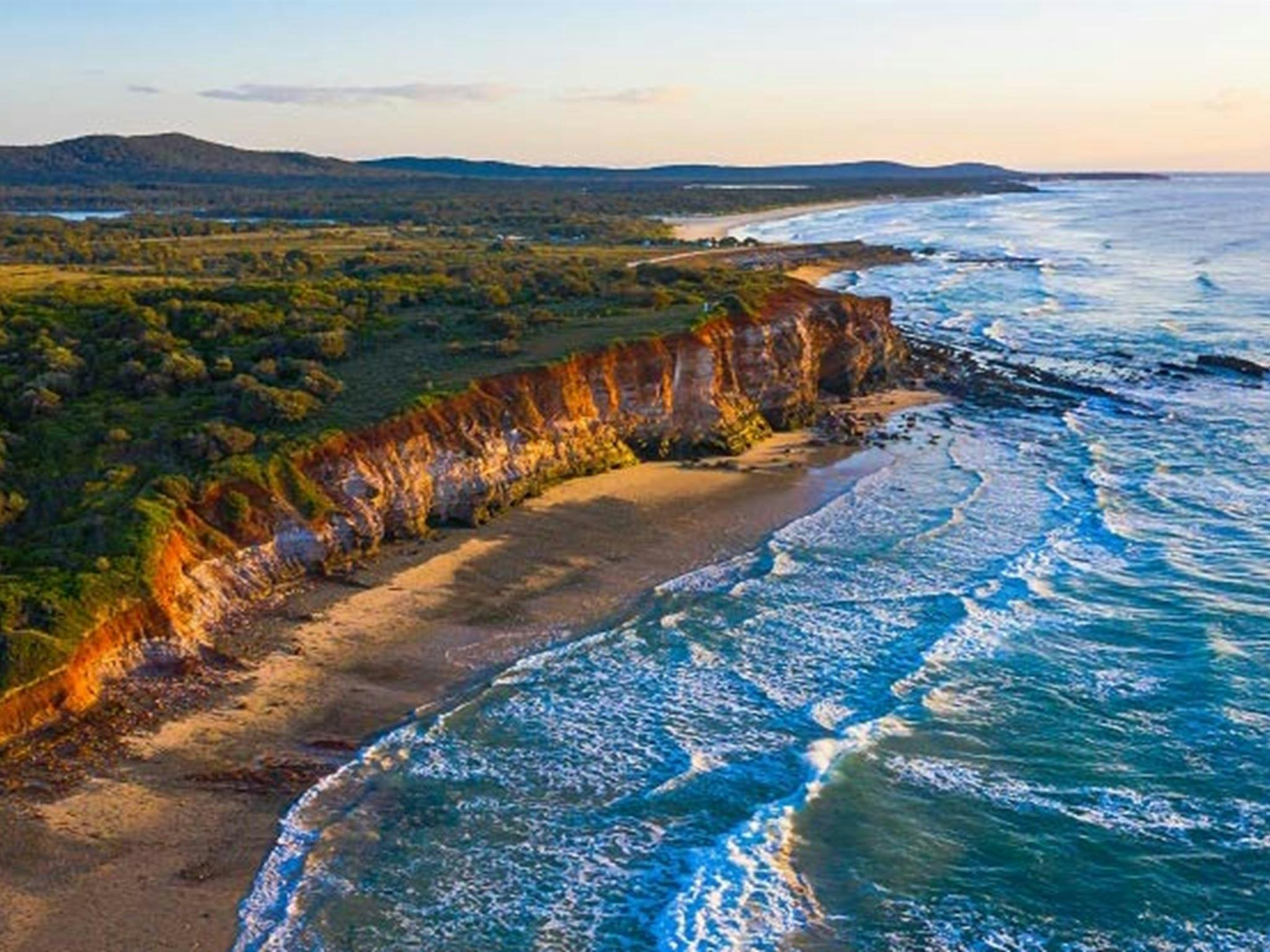 An aerial view of the red cliffs and ocean at Red Cliff campground in Yuraygir National Park. Photo: