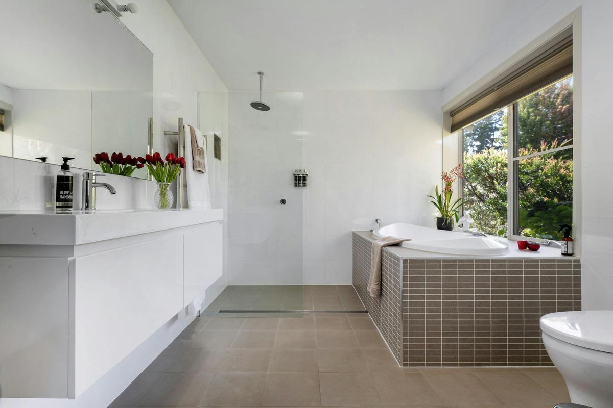 Full bathroom with walk-in shower, big bath under window with view of garden, toilet and vanity