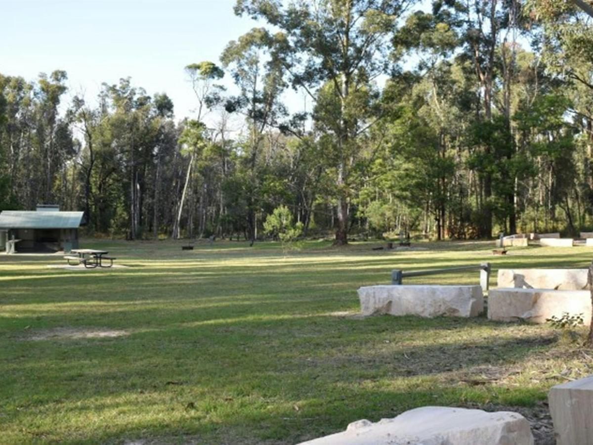A wide open grassy area with a picnic shelter in the distance at Mogo campground, Yengo National