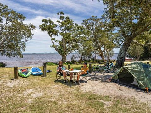 2 campers at a camping table near a tent by the water at Mungo Brush campground, Myall Lakes