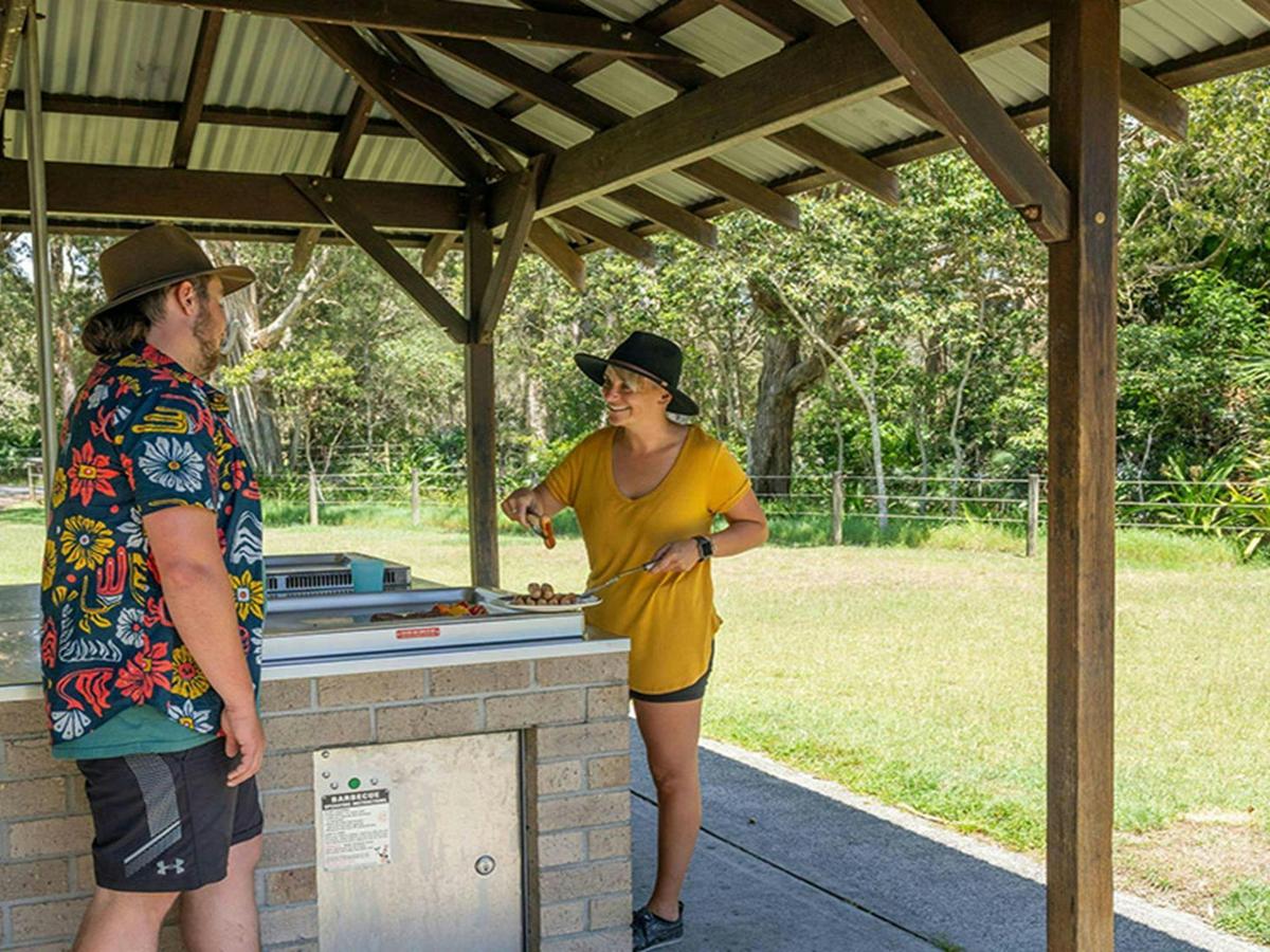 2 people cooking on a barbecue under a shelter at Mungo Brush campground, Myall Lakes National Park.