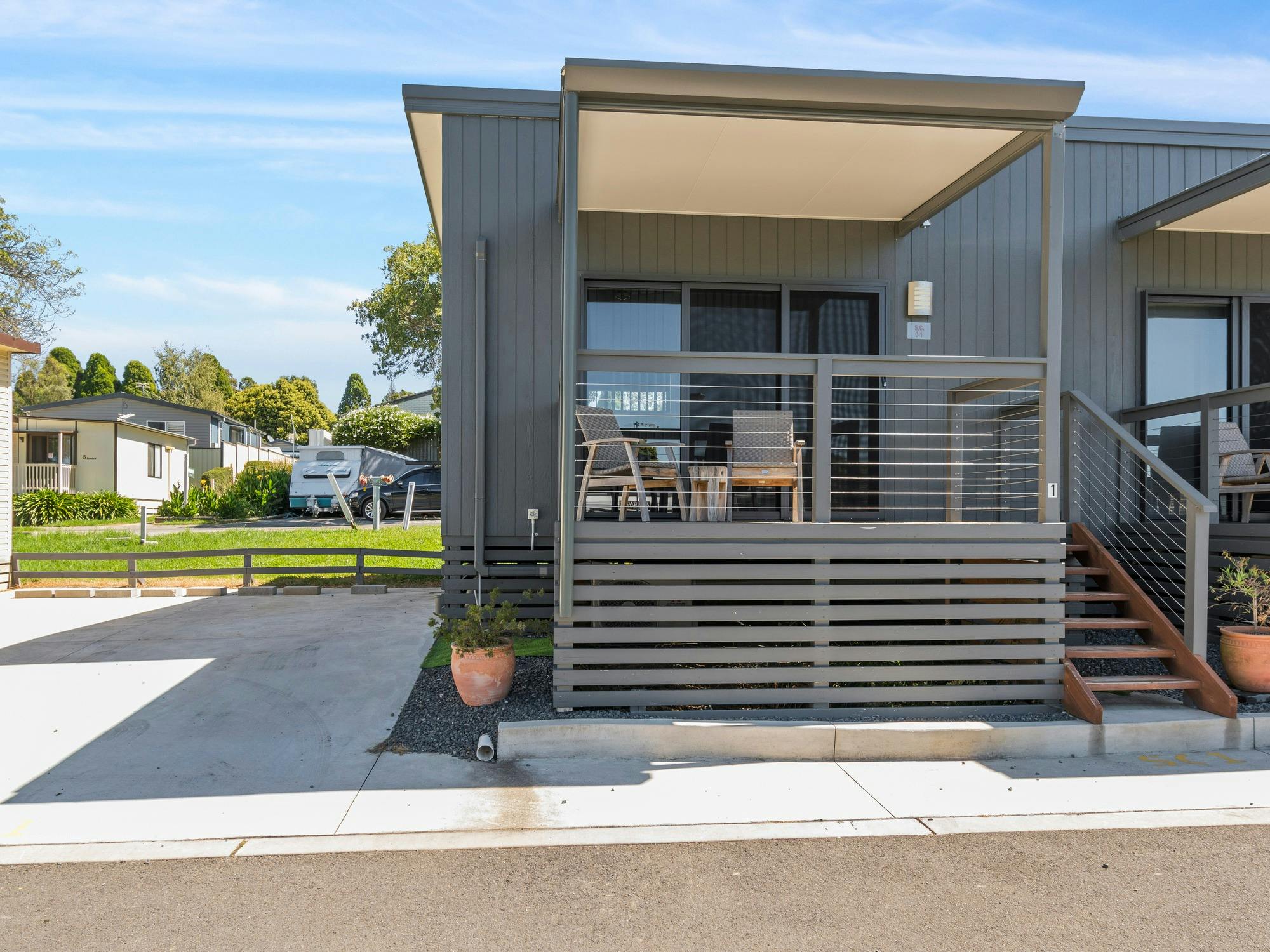 Modern cabin with a raised covered deck, outdoor seating, and sleek grey cladding.