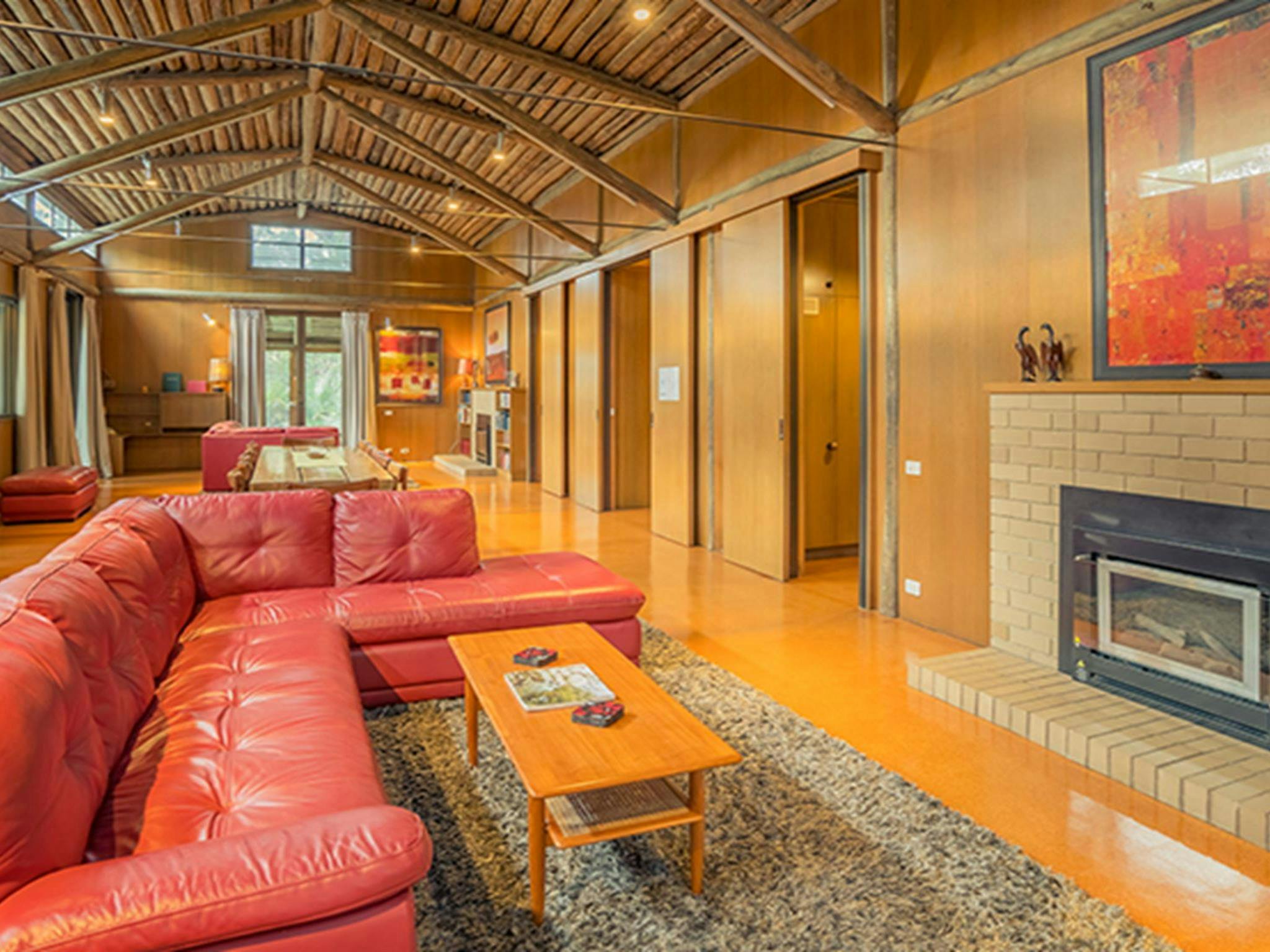 Red leather couch with a fire and rugs in the lounger room at Myer House. Photo: OEH/John Spencer