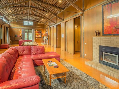 Red leather couch with a fire and rugs in the lounger room at Myer House. Photo: OEH/John Spencer