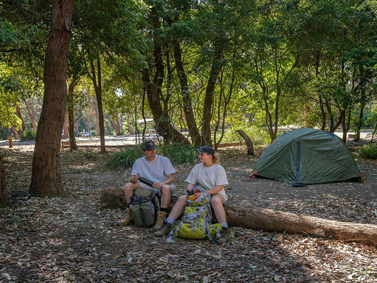Campers resting on a log at Pretty Beach campground. Credit: John Spencer &copy; DCCEEW