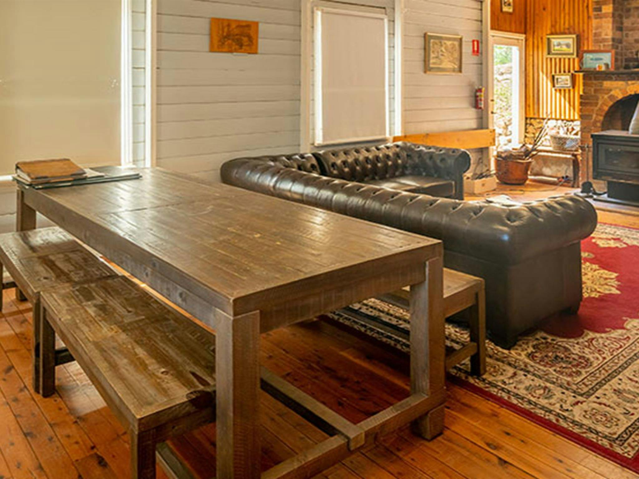 A long wooden dining table, sofa and wood heater at Post Office Lodge in Yerranderie Regional Park.