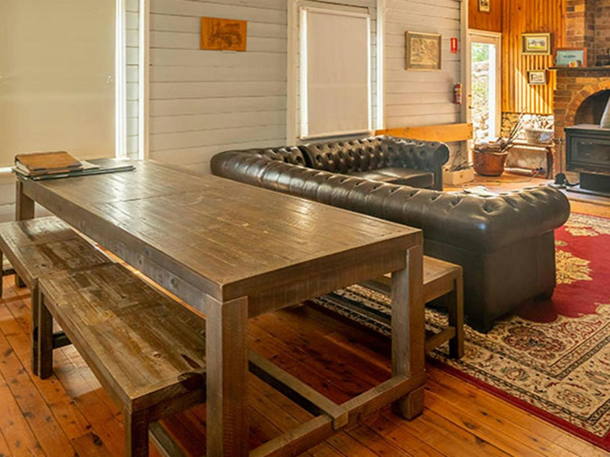 A long wooden dining table, sofa and wood heater at Post Office Lodge in Yerranderie Regional Park.
