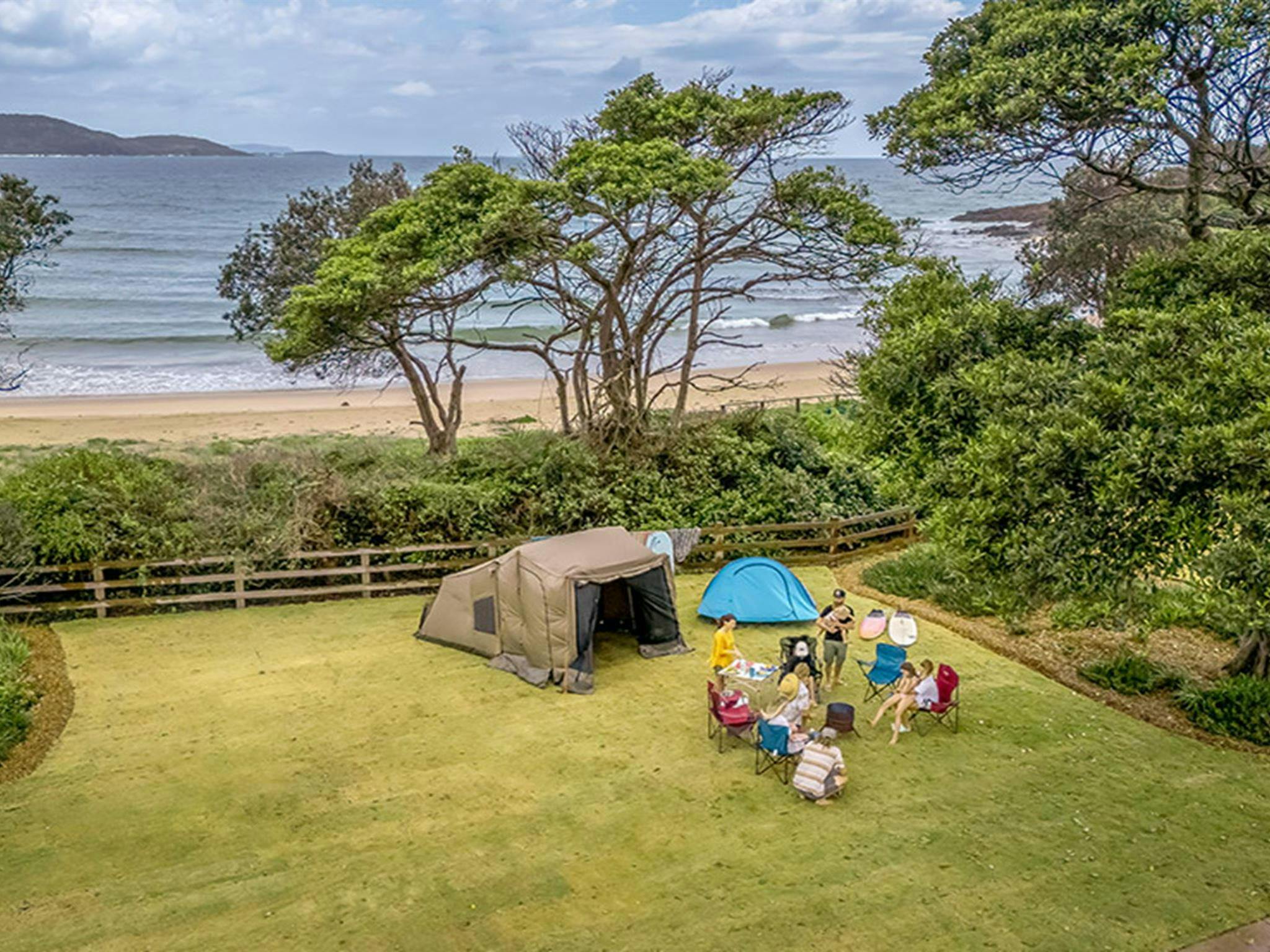 A family camping on a grassy site by the beach on the NSW north coast at Point Plomer campground in