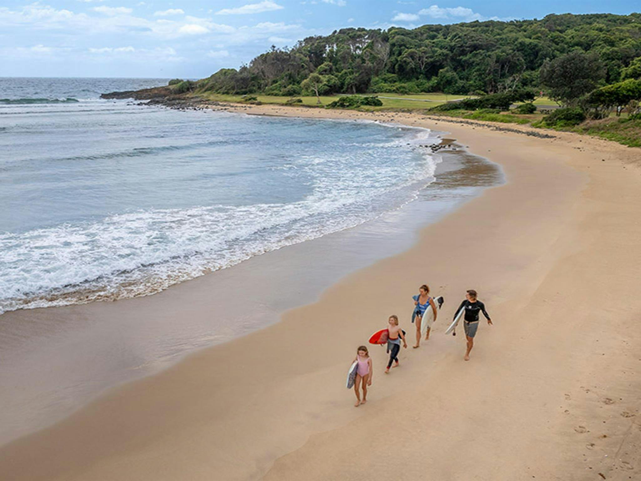A family walking the beach with surfboards under their arms, next to Point Plomer campground in