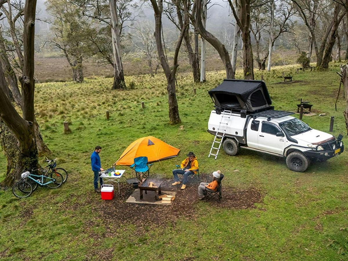 Campers around a wood barbecue next to a tent and a 4WD with a car tent in Polblue campground and