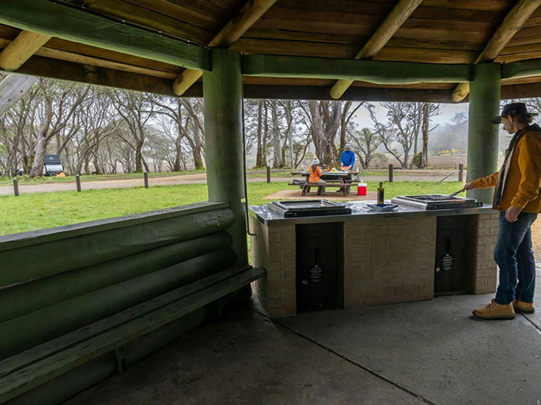 A person using a barbecue in a covered pavilion with views out to a picnic table in Polblue
