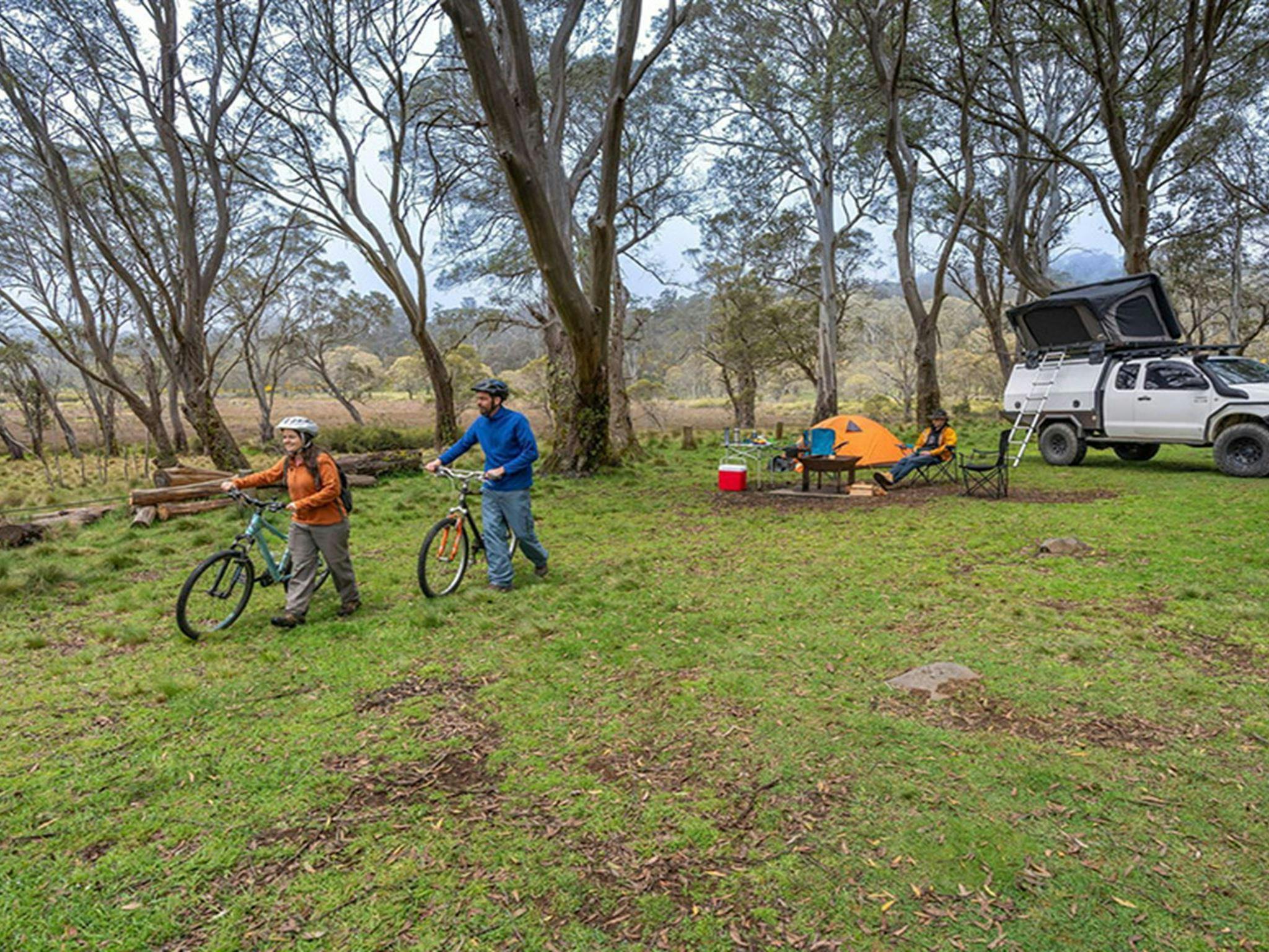 2 people walking mountain bikes from their campsite in Polblue campground and picnic area. Credit: