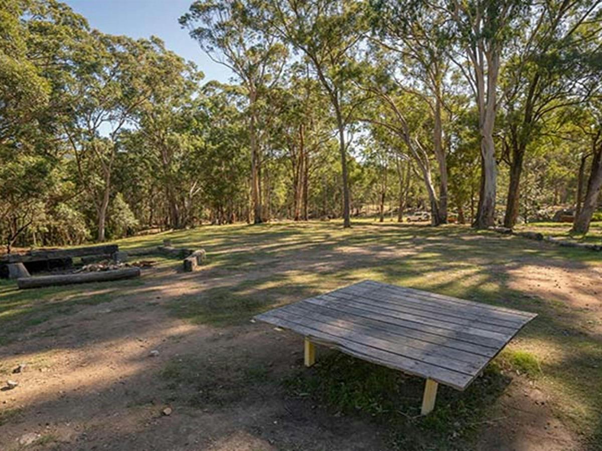 A wooden table with fire pit in the background, at Private Town campground in Yerranderie Regional