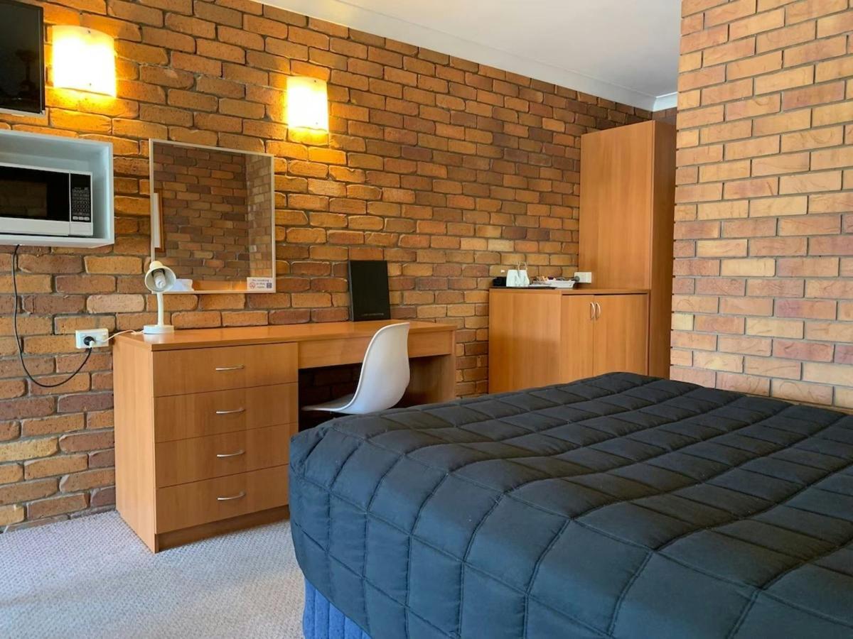 Bedroom with desk and kitchenette at Peter Allen Motor Inn