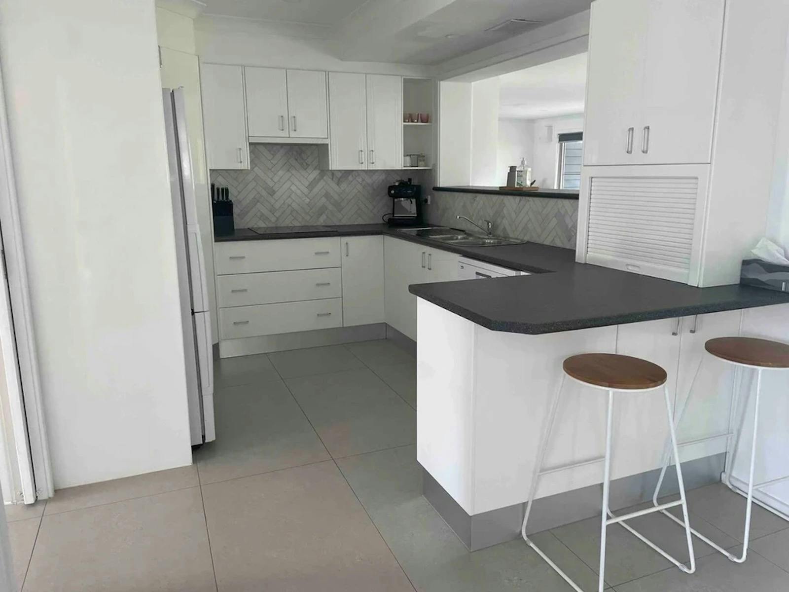 A modern kitchen with a clean, minimalist design. The floor is covered with large, light-grey tiles.