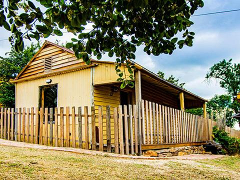 The exterior of Sydney Hotel Cottage surrounded by picket fence under trees in Hill End Historic