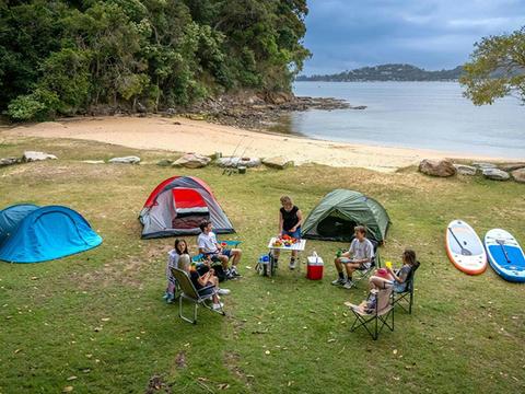 A group of campers sitting near their tents by the beach and bush at The Basin campground. Credit: