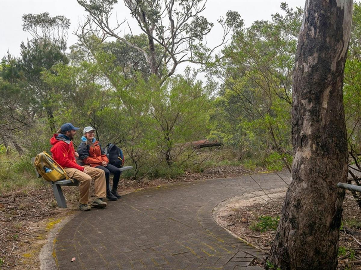 Two visitors stop for a rest and a chat on a seat beside the pathway from Adams lookout, Bungonia