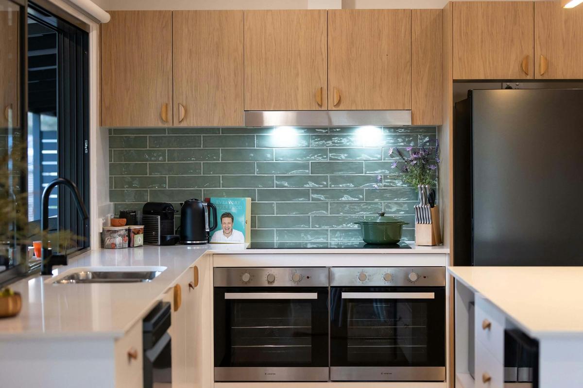 Modern kitchen with light wood cabinets, green subway tile backsplash, double ovens, black refridge