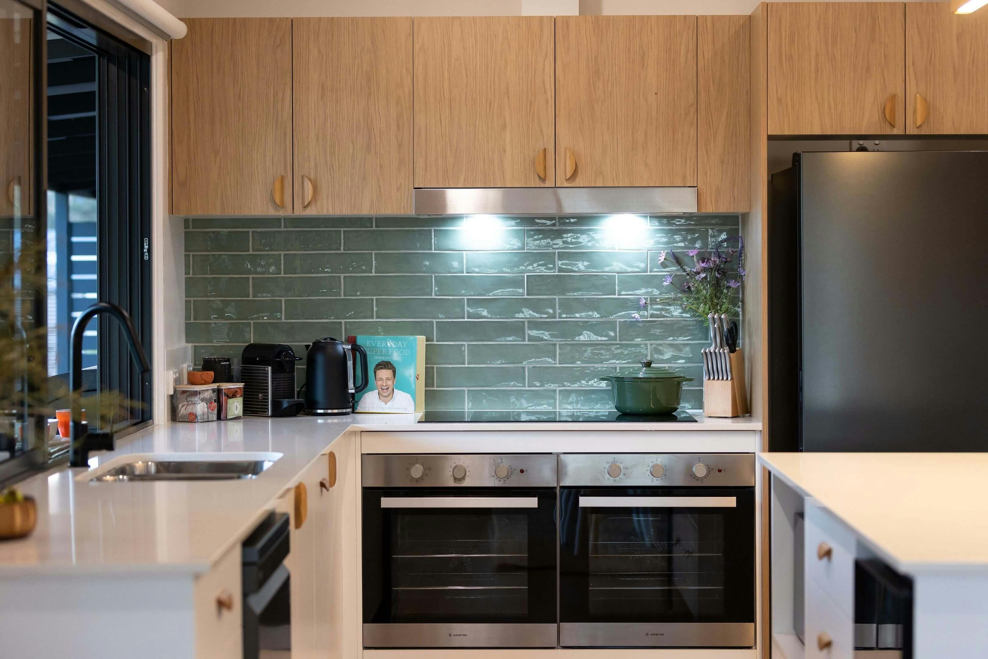 Modern kitchen with light wood cabinets, green subway tile backsplash, double ovens, black refridge