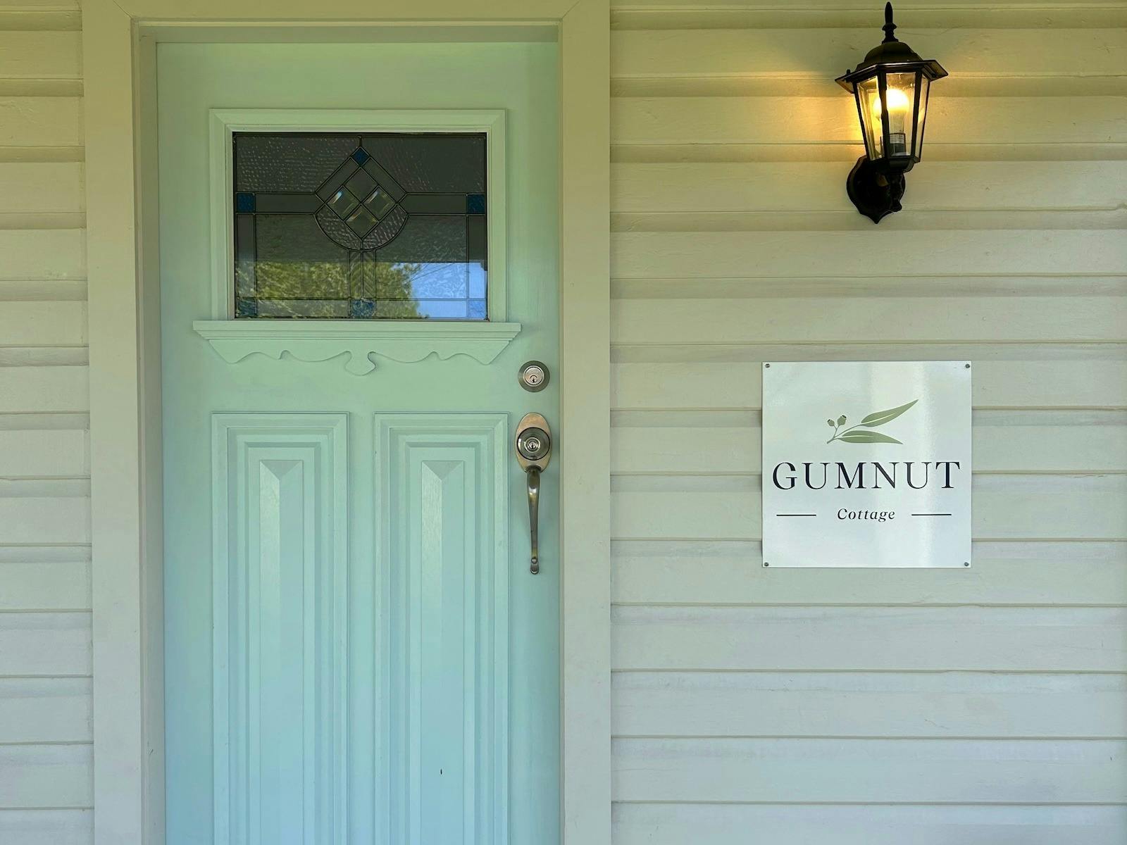 A blue door with stained glass, a lantern, and a sign reading "GUMNUT Cottage."