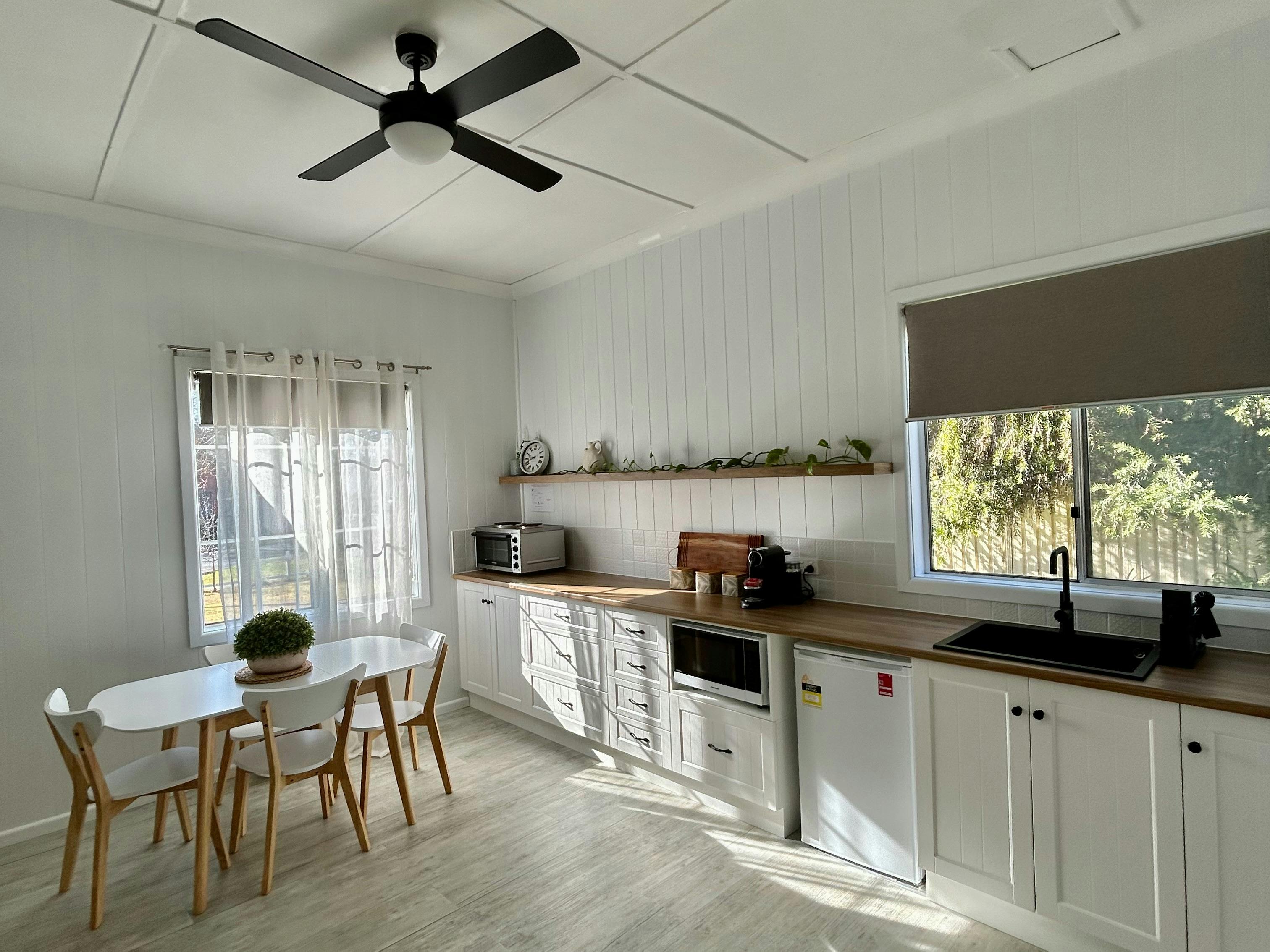 A bright kitchen with sun shining, white cabinets, fridge, microwave, oven, sink, and dining table.