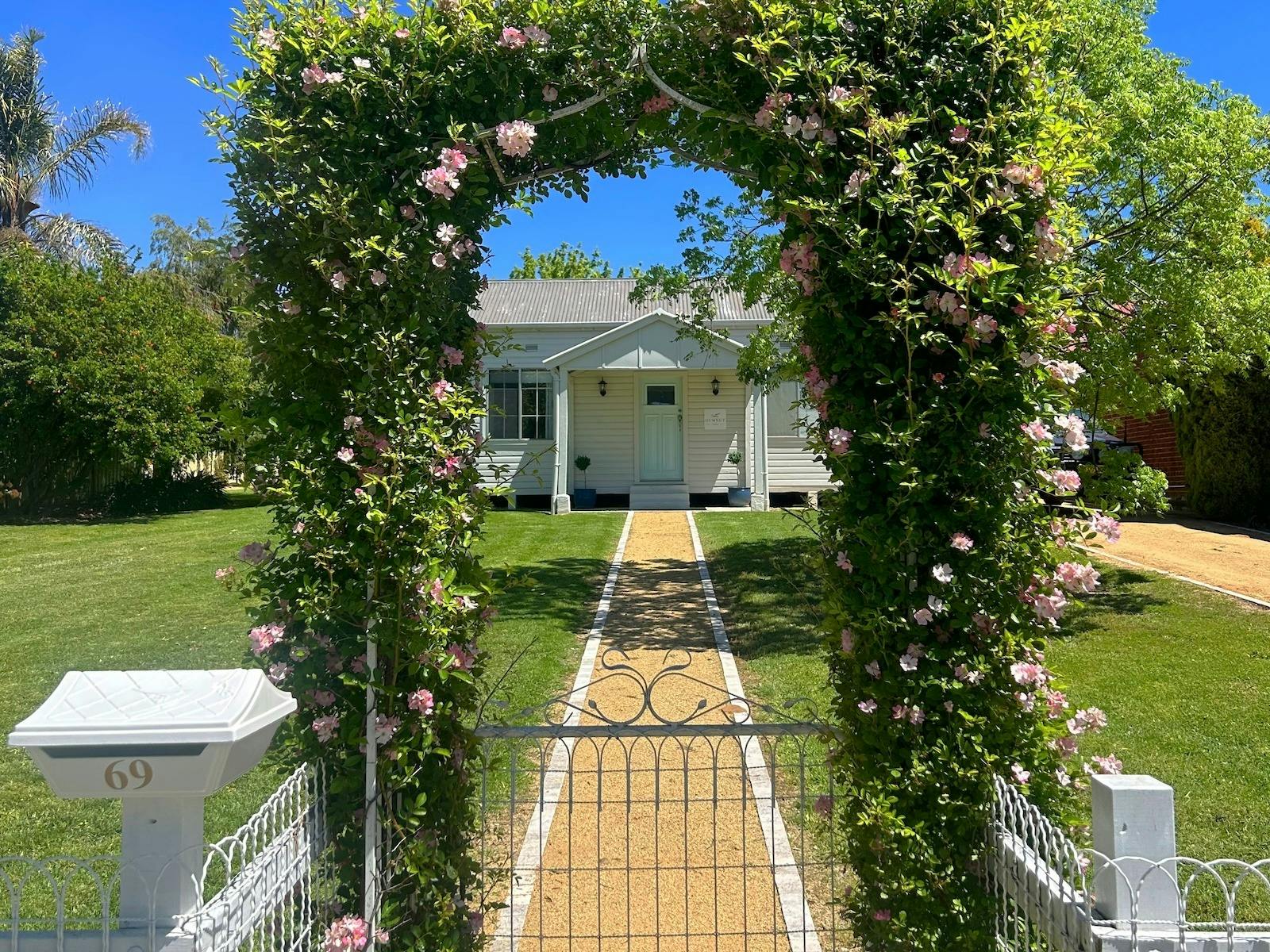 A charming cottage with a blue door, framed by a flowering vine archway and a garden path.