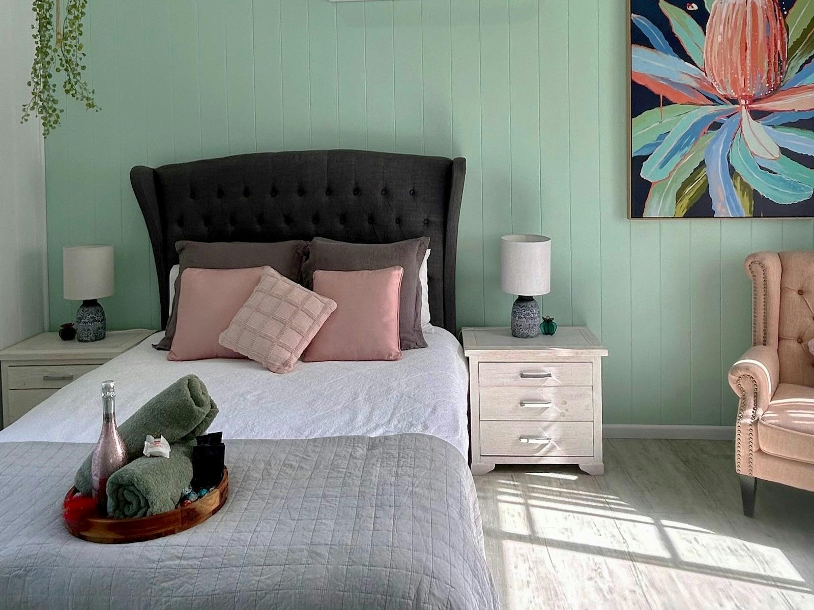 A cozy bedroom for two with pastel pink cushions, mint green walls, and vibrant floral artwork.
