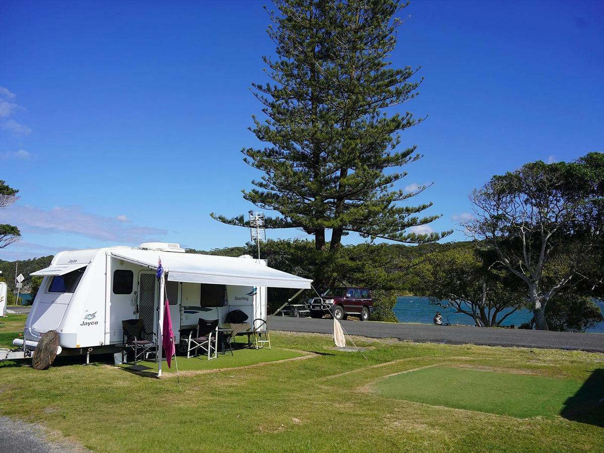 Caravan parked on artificial turf pad near the river at Wooli holiday park