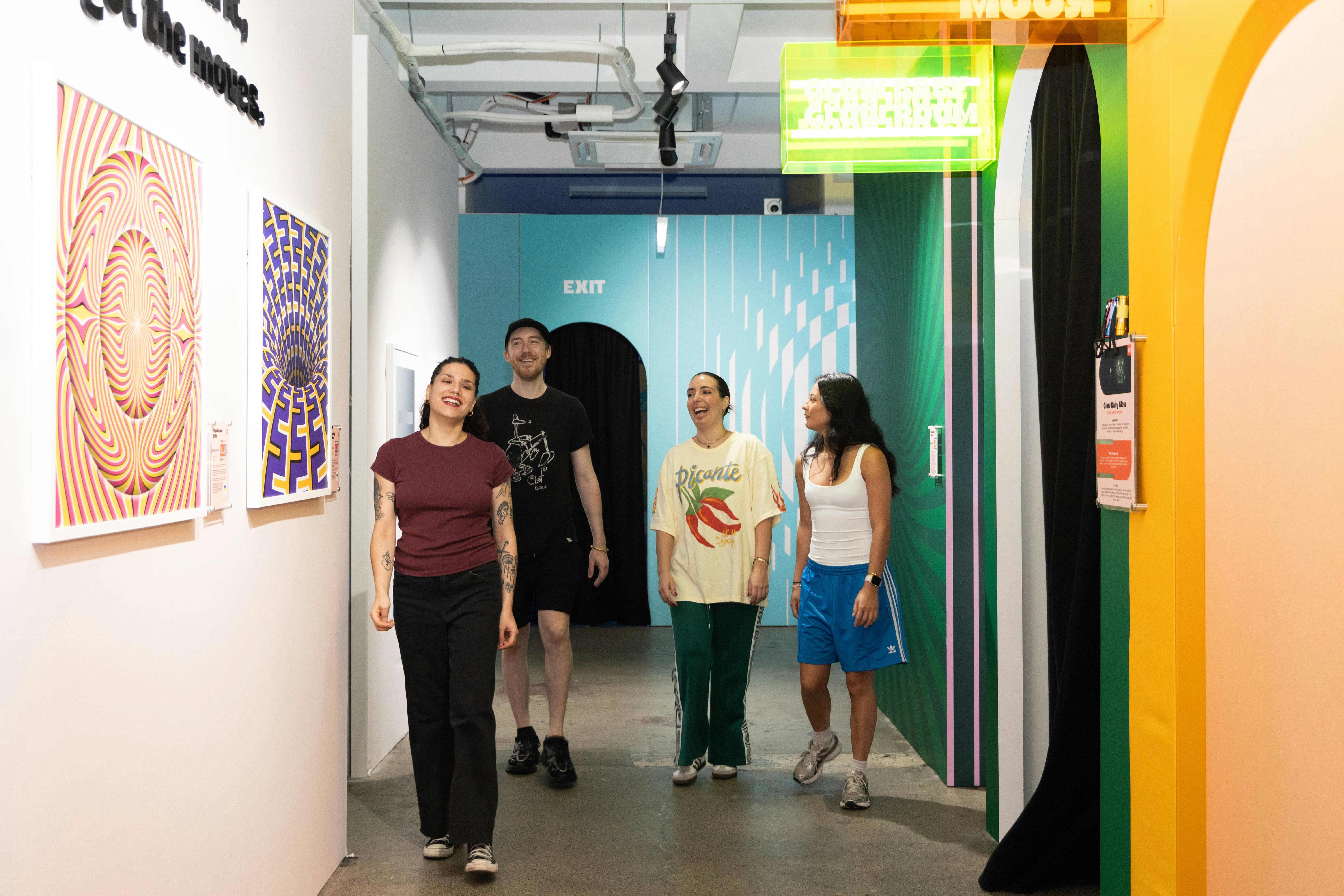 Four people walk cheerfully through a colorful art exhibit with vibrant patterns on the walls.