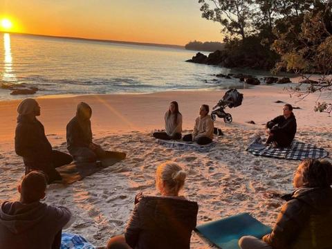 Group sitting around in a circle on the beach doing breathwork