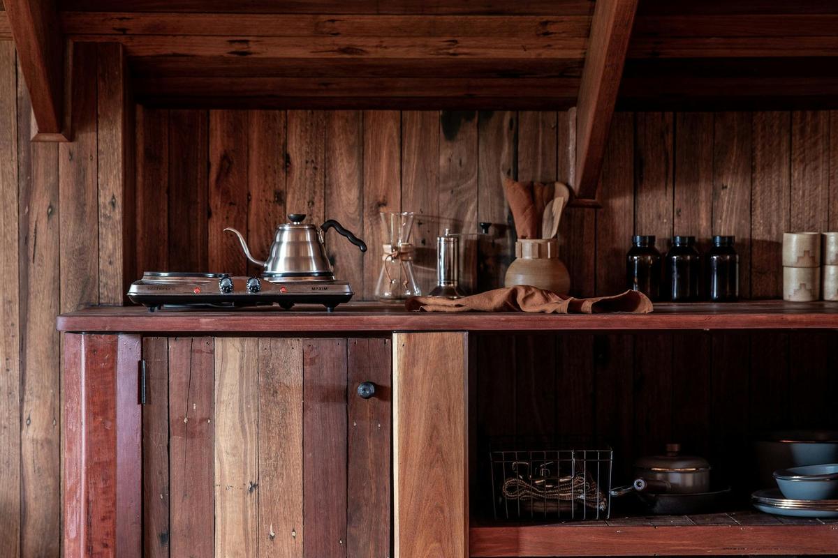 A small camp stove top with a few pots and pans, a kettle and ceramic mugs and a Chemex coffee pot.