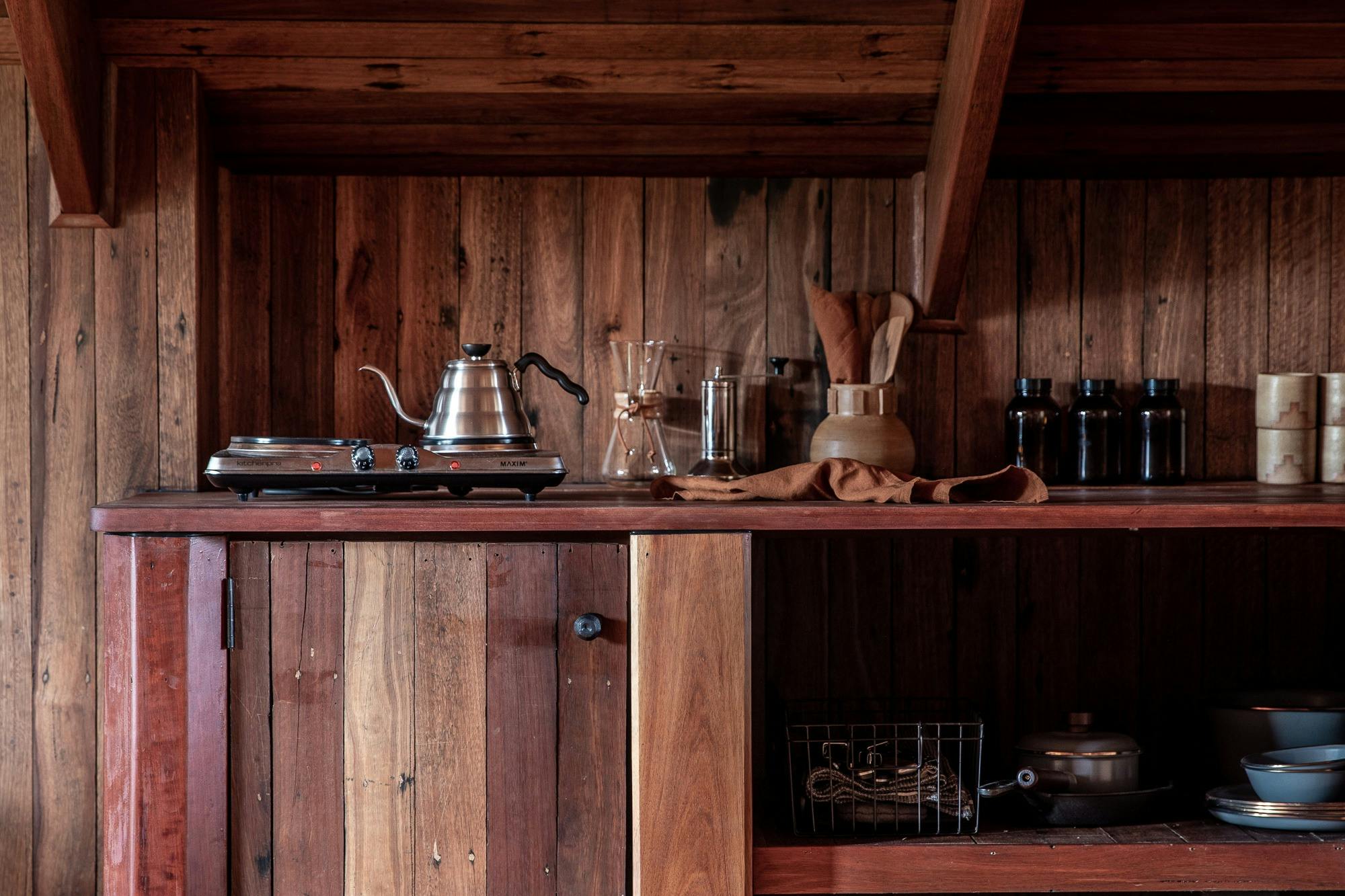 A small camp stove top with a few pots and pans, a kettle and ceramic mugs and a Chemex coffee pot.