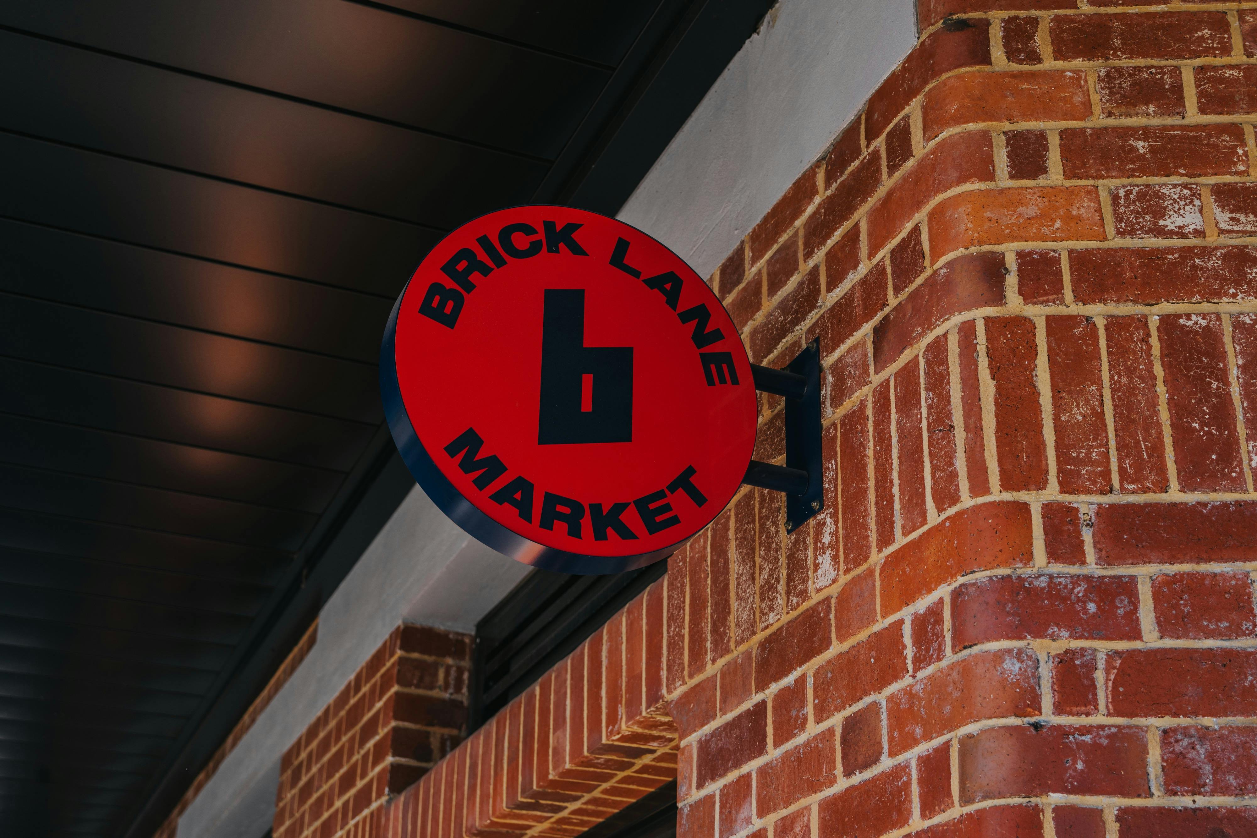 Red circular "Brick Lane Market" sign with navy blue text, mounted on a red brick wall