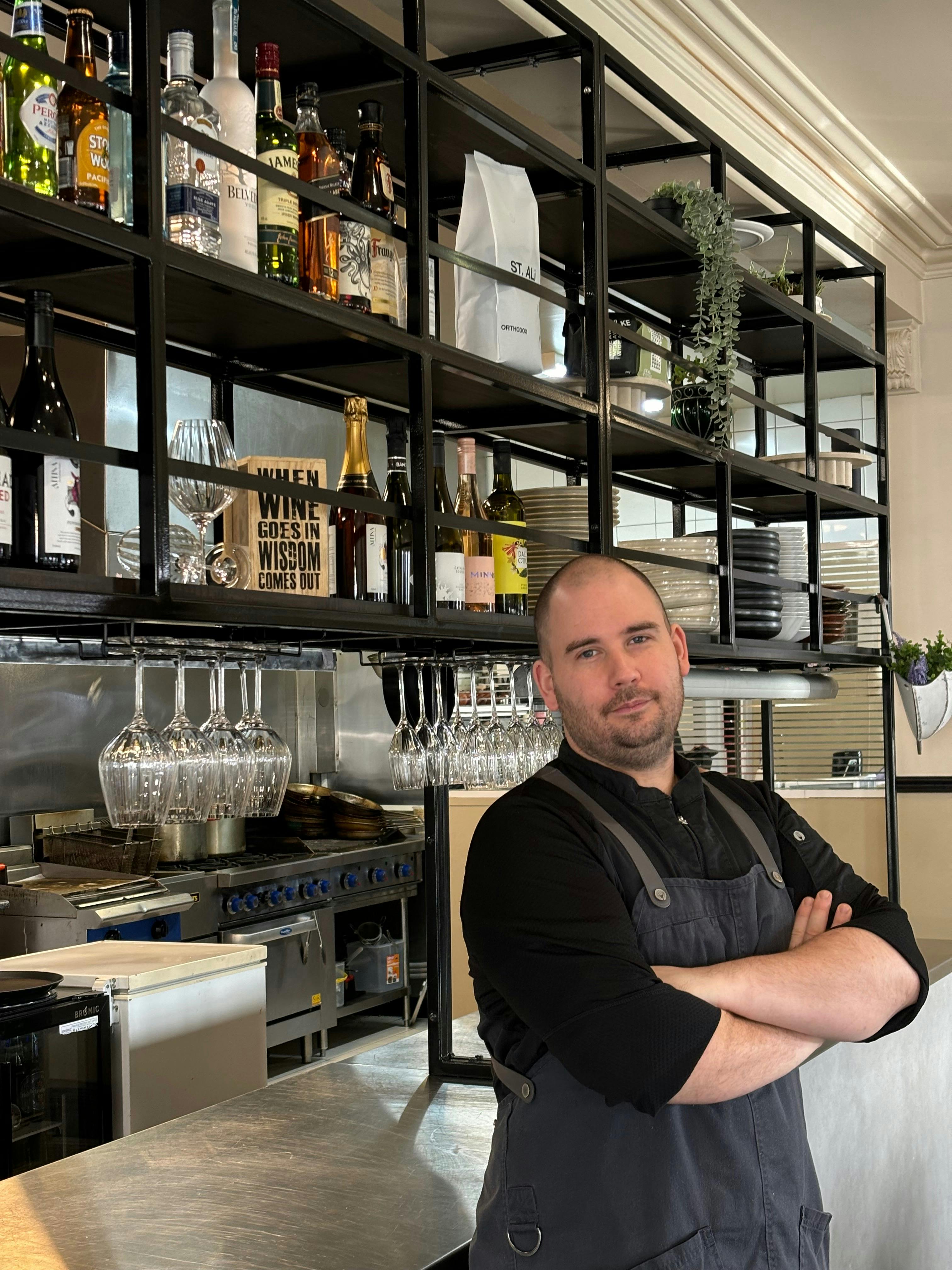 Head Chef Kevin Roberts in front of restaurant bar and pass.